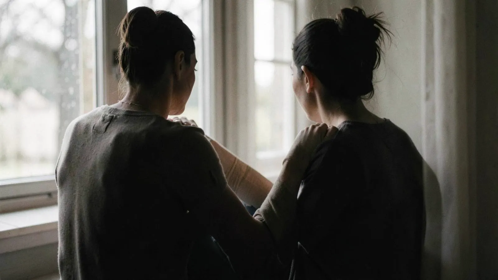 Injured person seated by a window with a family member offering support